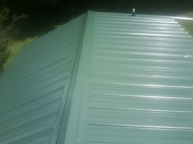 New green metal panels meeting at the ridge of a roof — Flat Roof Repair work by our crew in Minneapolis